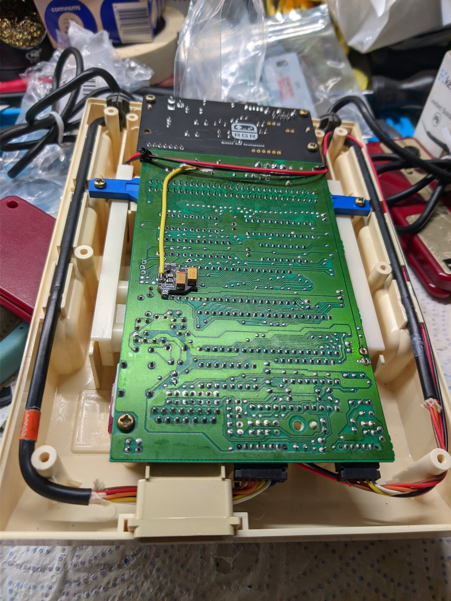 Famicom motherboard installed in beige plastic case with composite mod board mounted above, blue heatsinks visible, power wiring connected with red/black cables.
