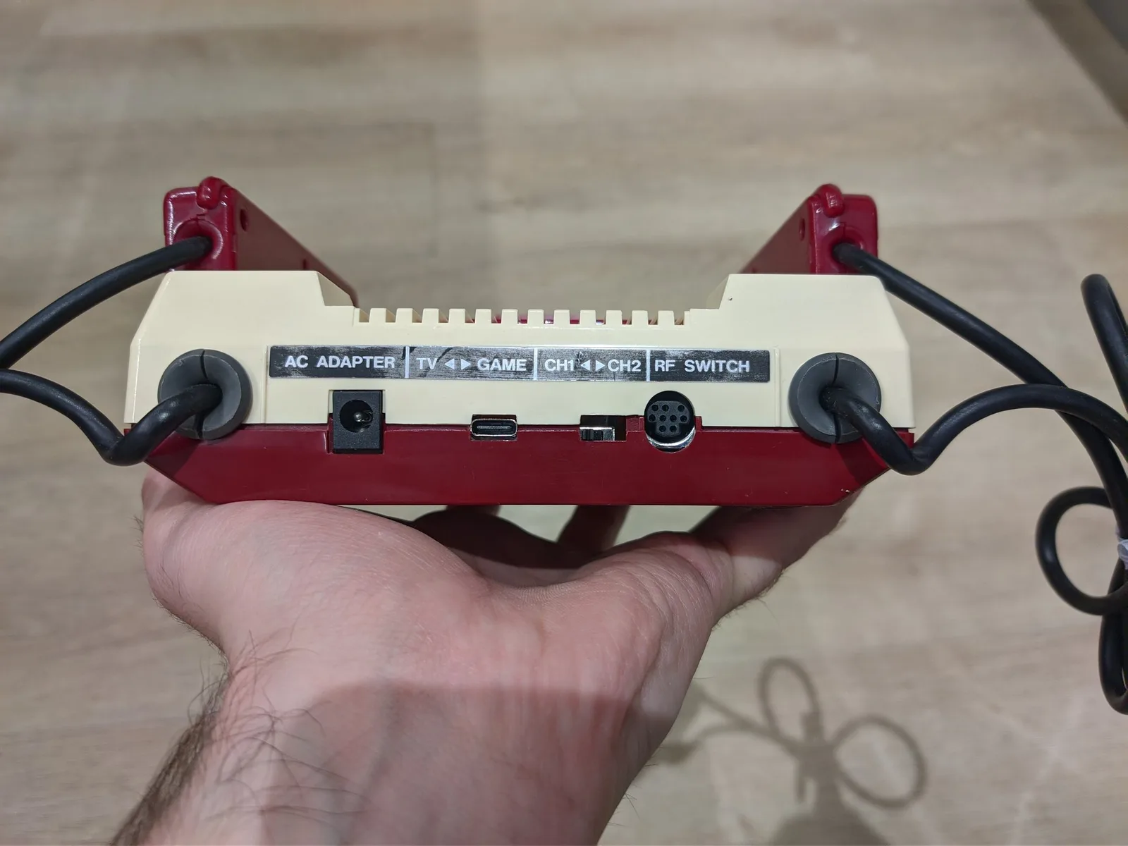 Famicom rear panel showing composite adapter with AC adapter, TV/Game, channel switches, and RF switch ports visible in hand.