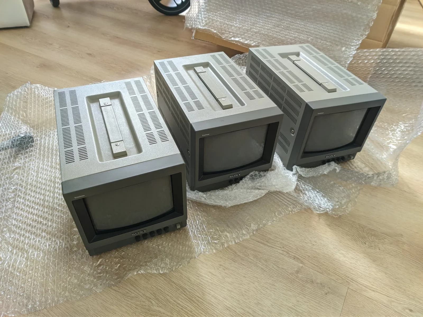 Three Sony PVM-9040 CRT monitors still in bubble wrap packaging, showing exterior casing damage from shipping from Japan.