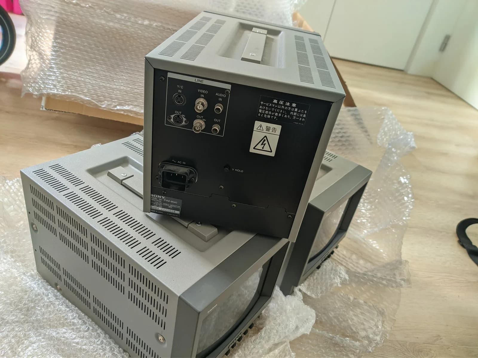 Sony PVM-9040 monitor with back panel visible showing video/audio connections, AC inlet, and warning labels; unit wrapped in bubble wrap.