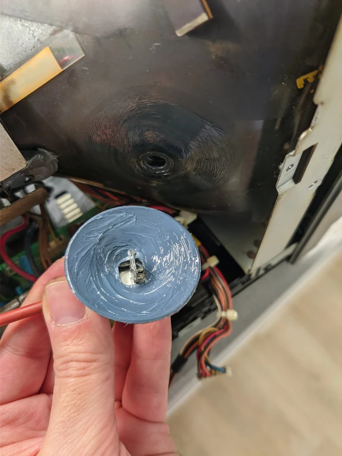 Blue anode cap held in hand showing reflowed solder joint, with CRT monitor and internal components visible in background.