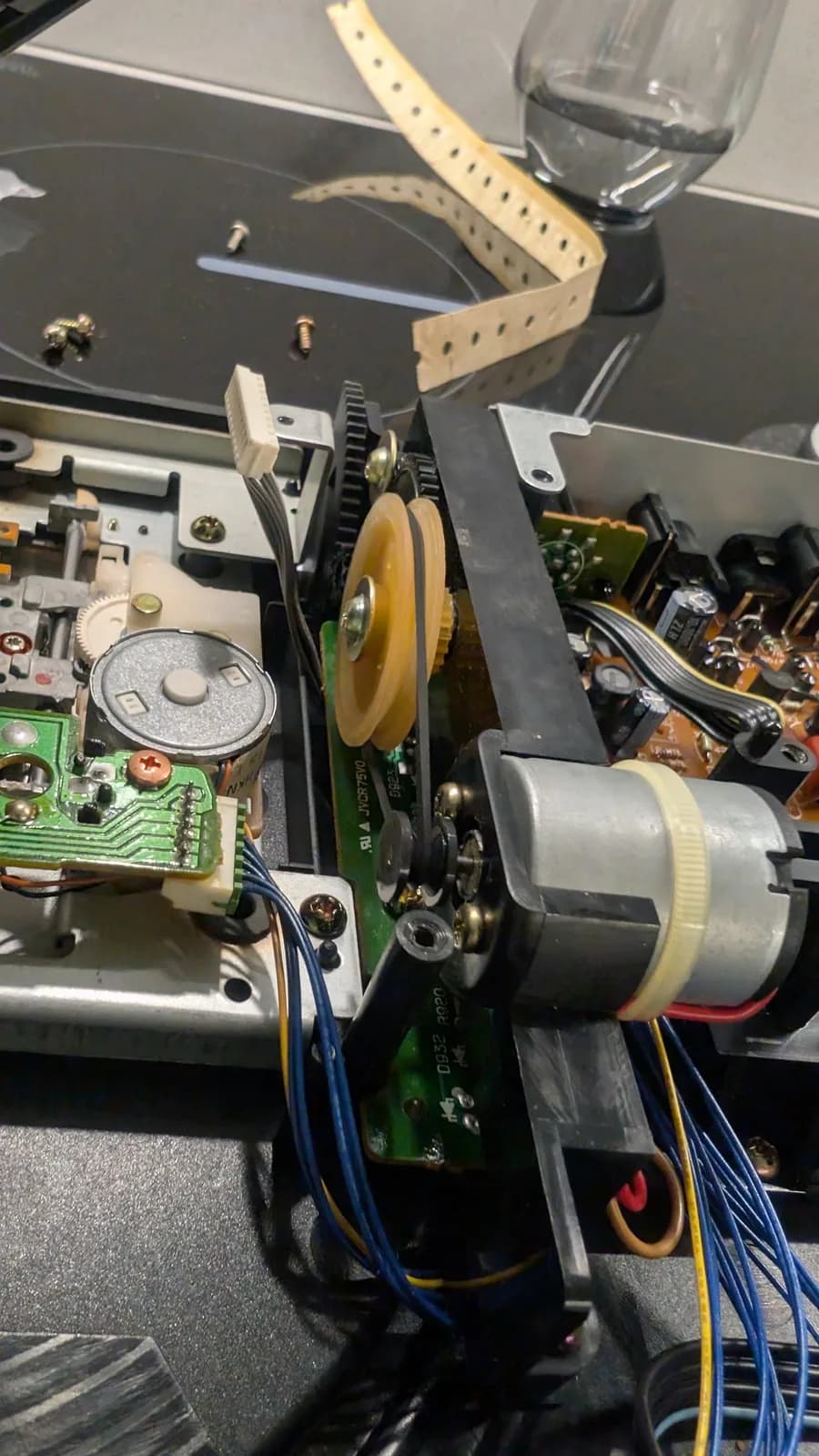 Sega Wondermega open chassis with the new CD drive belt fitted around the motor pulley and the cream flywheel, beside the laser sled and a servo PCB (JVC R75VO).