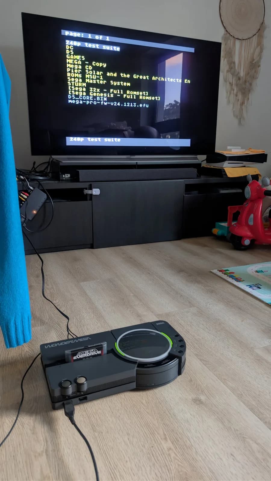 Restored Sega Wondermega HWM-5010 on the floor with a Mega Everdrive Pro flashcart inserted, the LG C1 OLED TV behind showing the Everdrive Pro file menu with "240p test suite" highlighted.