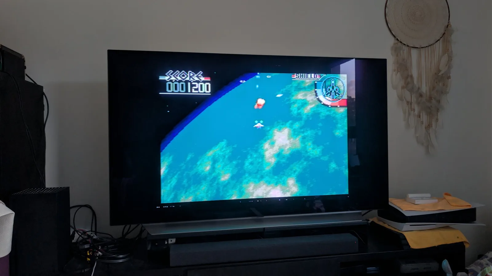 LG C1 OLED TV displaying the Mega-CD shooter Silpheed, the player craft flying over a rendered, mostly blue planet, with SCORE 0001200 and a SHIELD gauge in the HUD.