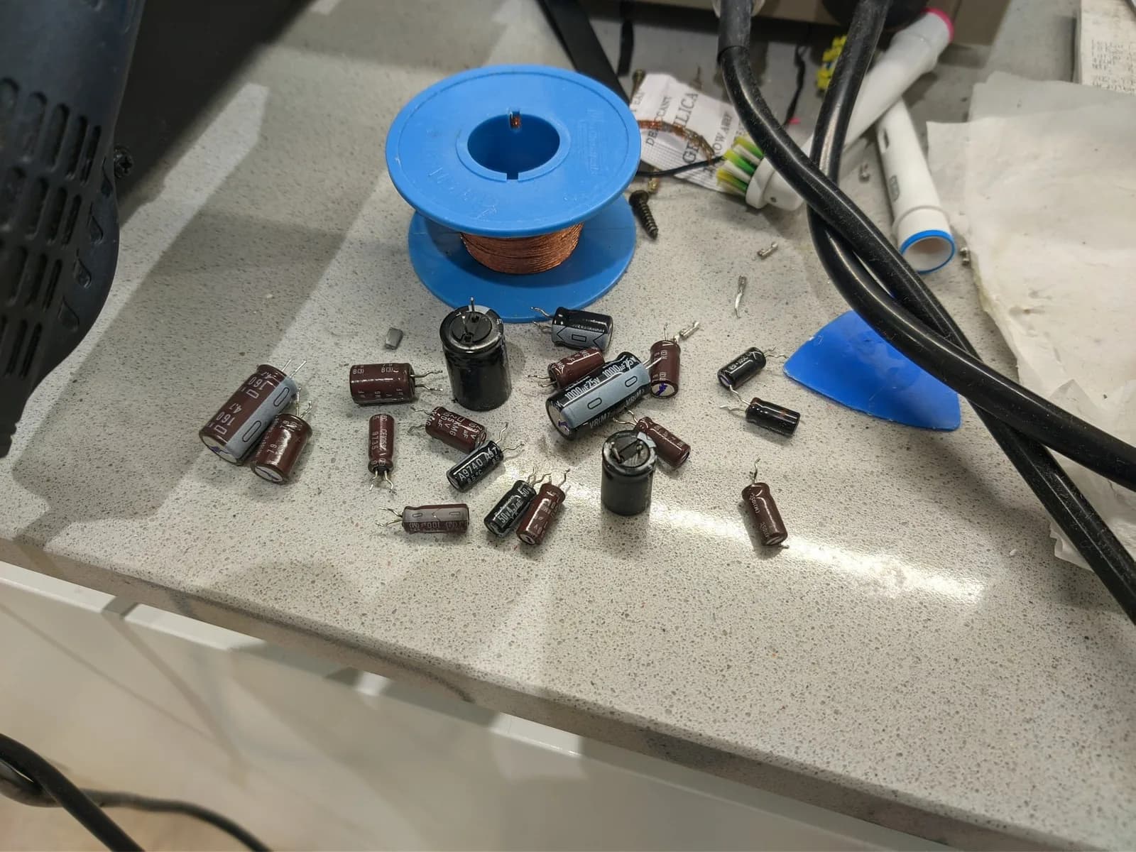 Disassembled electrolytic capacitors and components from Sony PVM-14M4J, including cylindrical caps, resistors, and a spool of copper wire on workbench.