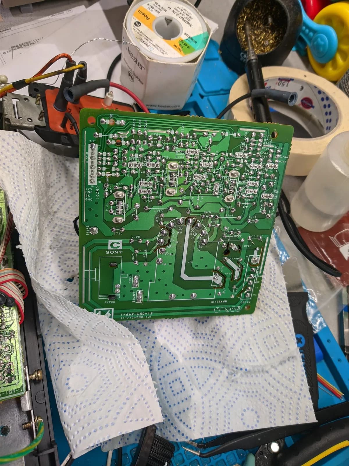 Sony PVM-14M4J C board PCB with reflowed solder joints on workbench, surrounded by repair tools and supplies.