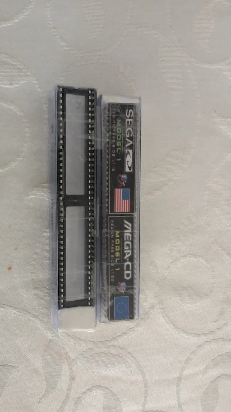 Sega Mega-CD Model 1 unit in clear plastic case showing internal circuit board with dual rows of pin connectors, displayed on textured surface.