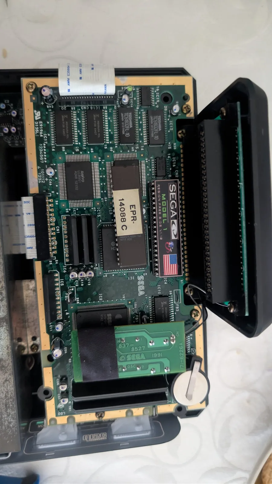 Sega Mega-CD 1 mainboard with SEGACD and ERR 4088C chips visible, yellow daughterboard attached, undergoing region unlock modification.