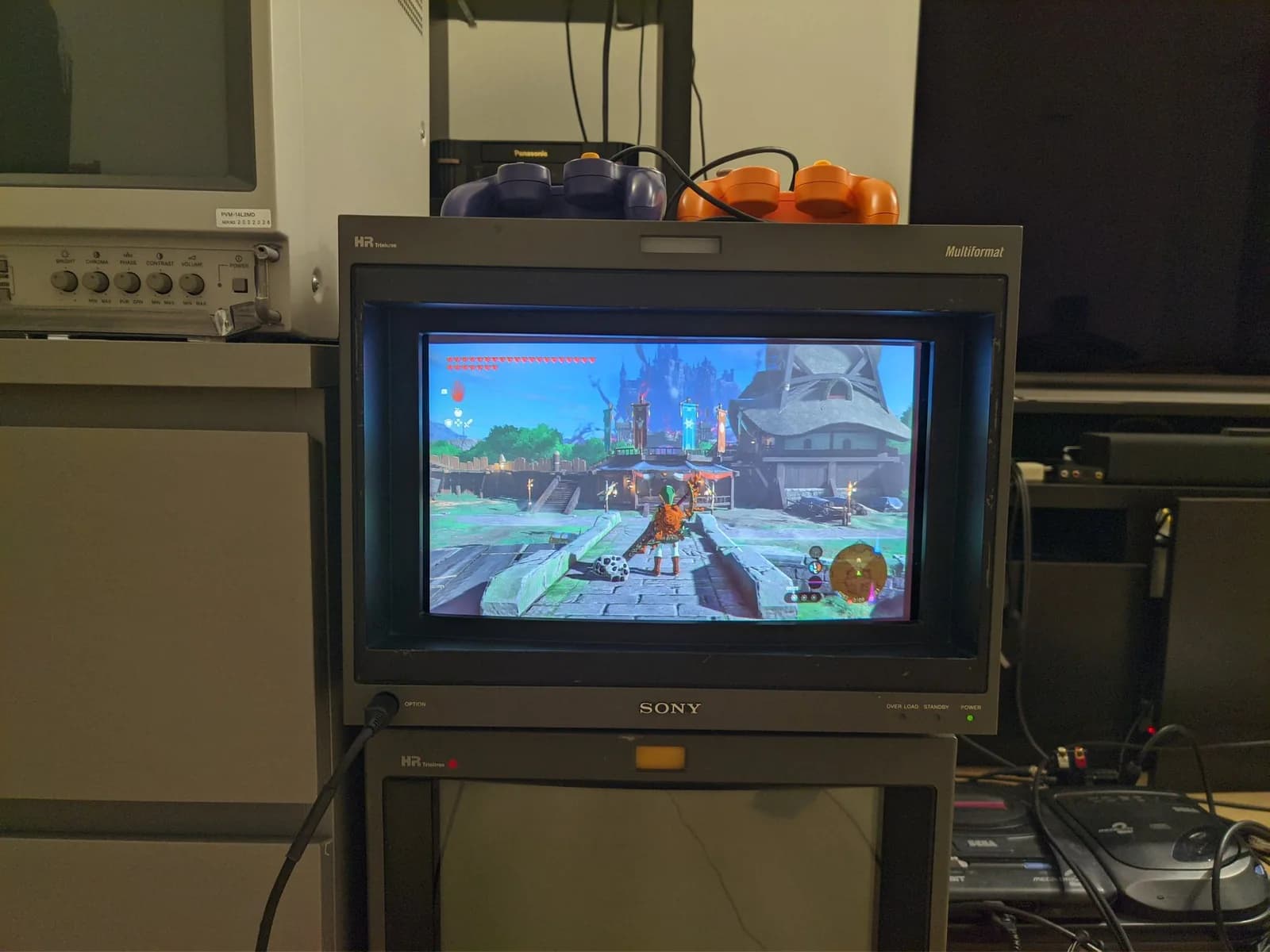 Sony BVM-D14H1E showing The Legend of Zelda: Tears of the Kingdom gameplay at Lookout Landing (the game's main hub area), two GameCube controllers resting on top.