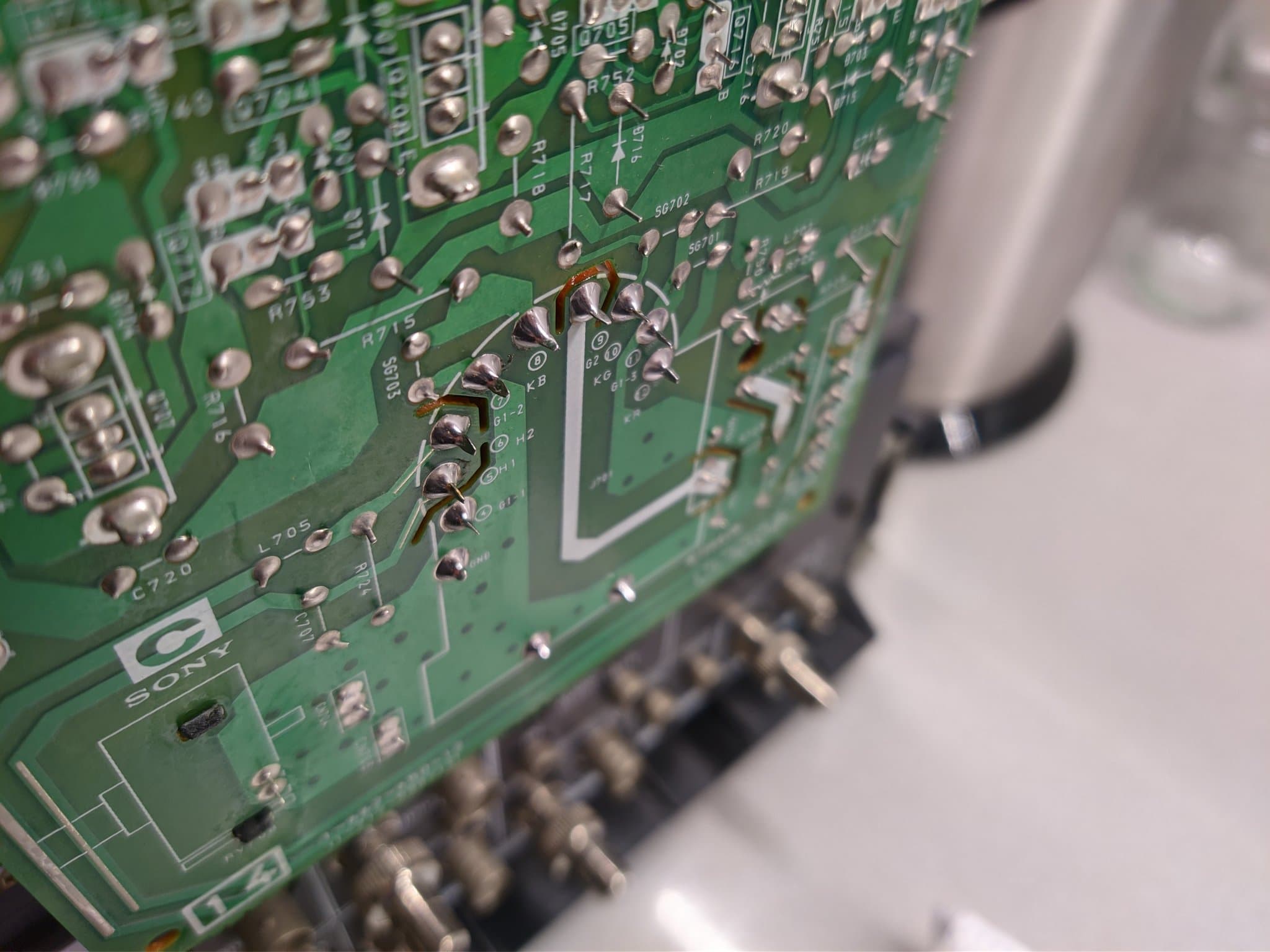 Close-up of Sony PVM-14M4J C board showing broken solder joint at KB tube pin with multimeter probe testing connection.