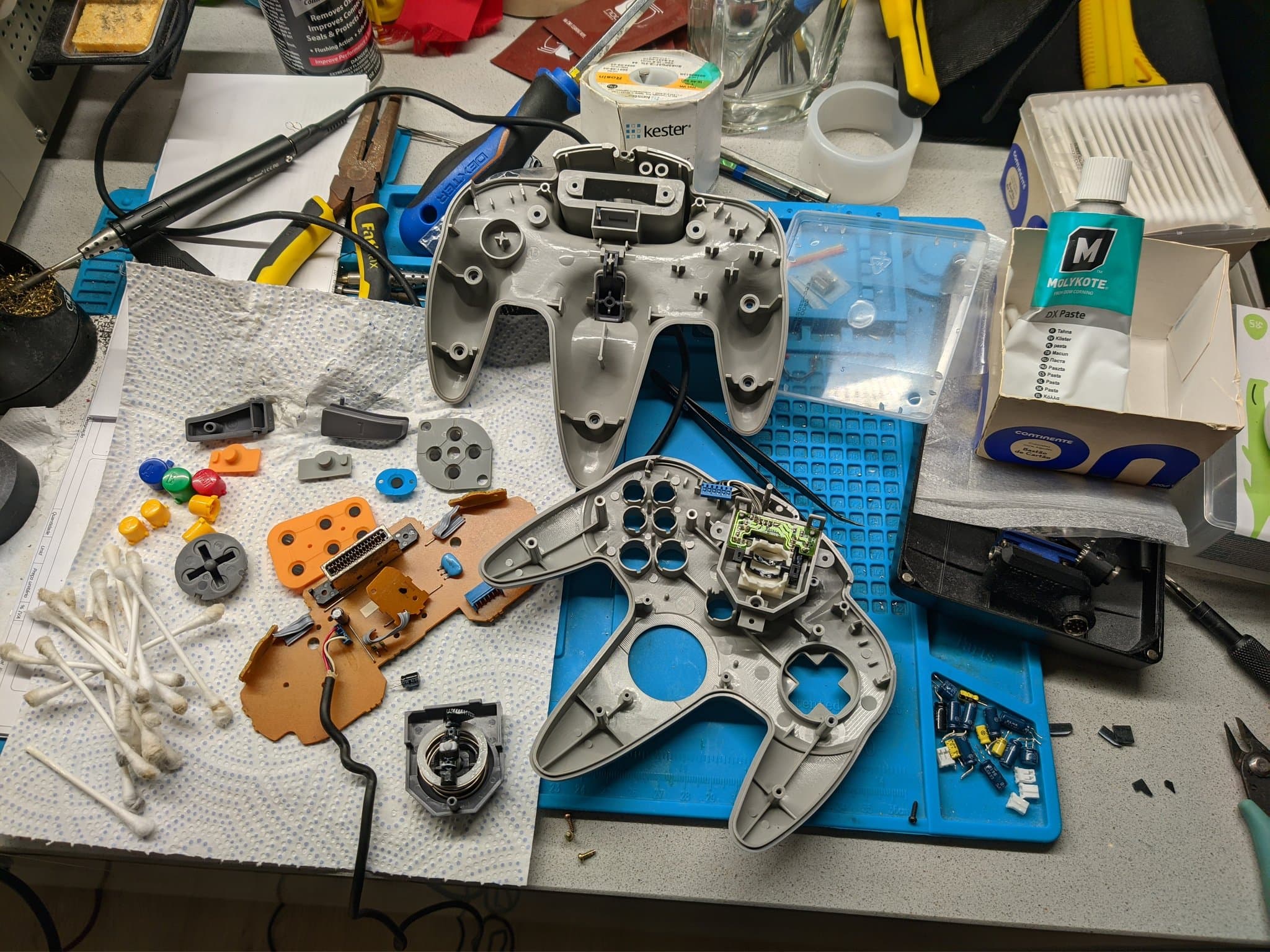 Disassembled N64 controller parts laid out on a blue silicone mat: membranes, buttons, joysticks and shells, during the controller overhaul.