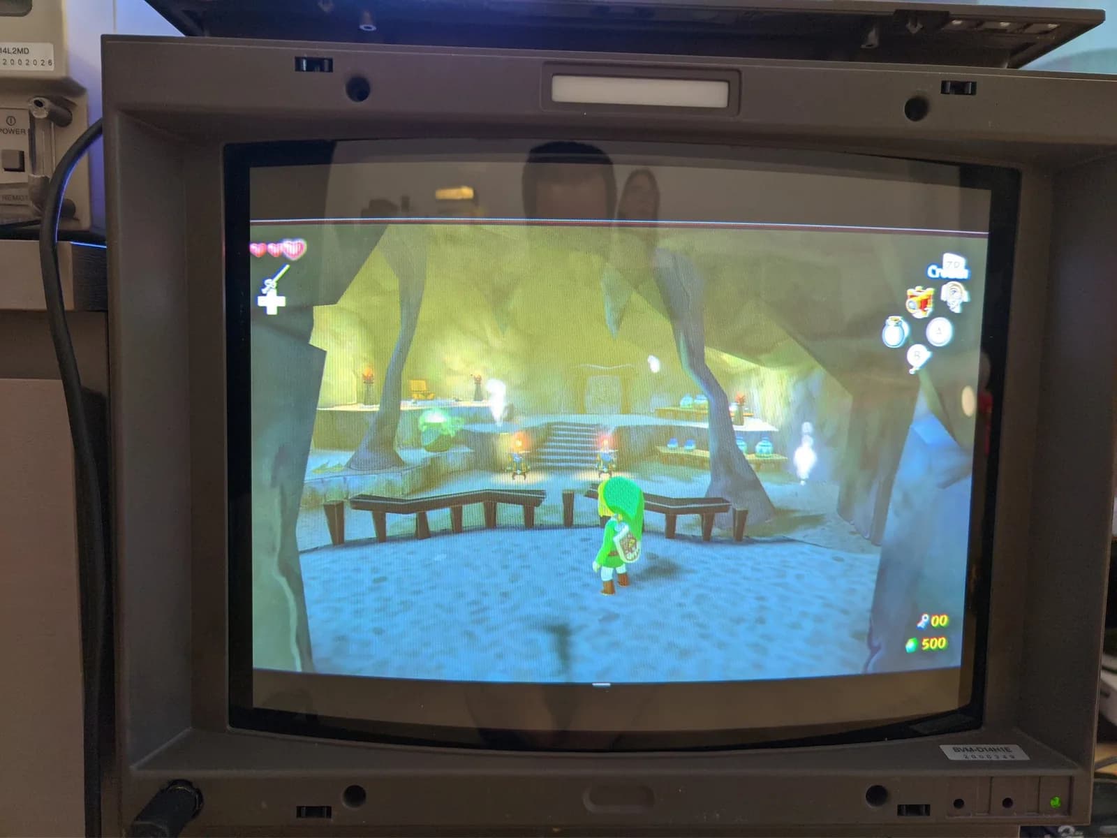 The Legend of Zelda: The Wind Waker HD gameplay on the Sony BVM-D14H1E (model label visible on the bezel), Link in a green tunic in a dimly lit cave interior with wooden railings and stone stairs, from a Wii U at 1080i.