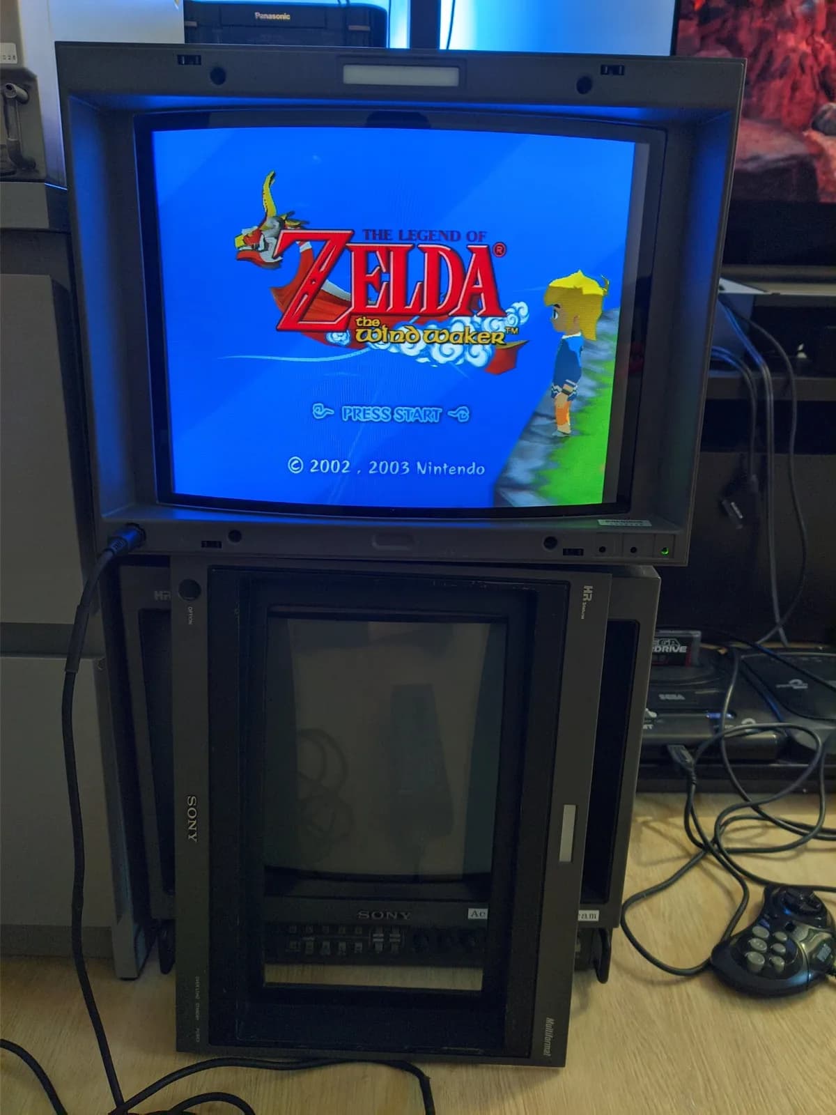 Sony BVM-D14H1E on top showing The Legend of Zelda: The Wind Waker in full 4:3, its own front fascia (carrying the 16:9 mask) removed and propped in front, stacked above a Sony PVM-14M4J monitor.