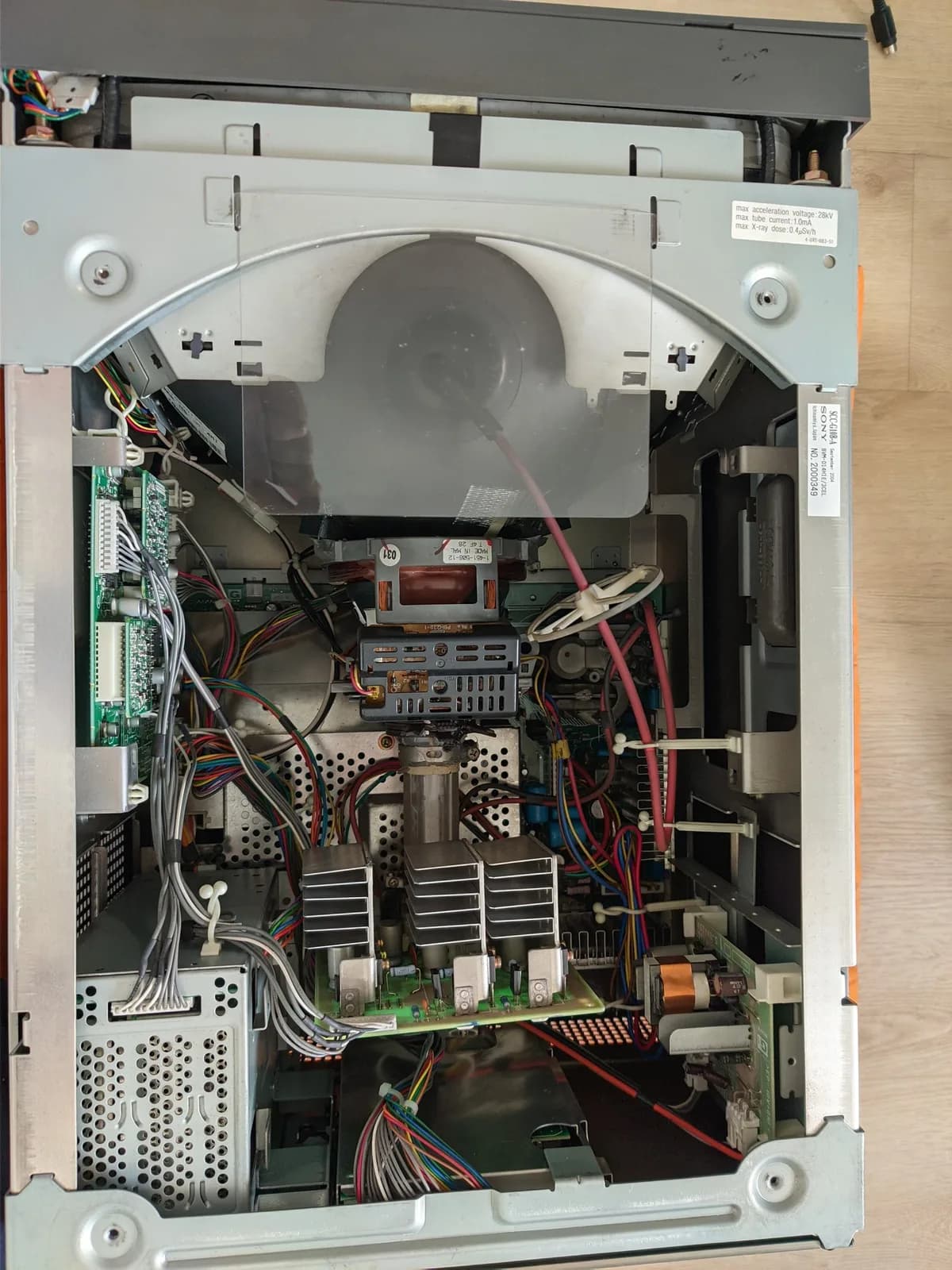 Interior of the Sony BVM-D14H1E with the cover removed: green circuit boards, a copper-wound coil, and three finned heatsinks on the CRT neck board (likely the R, G and B video amplifiers), with red high-voltage anode leads and colourful wiring around the tube neck.