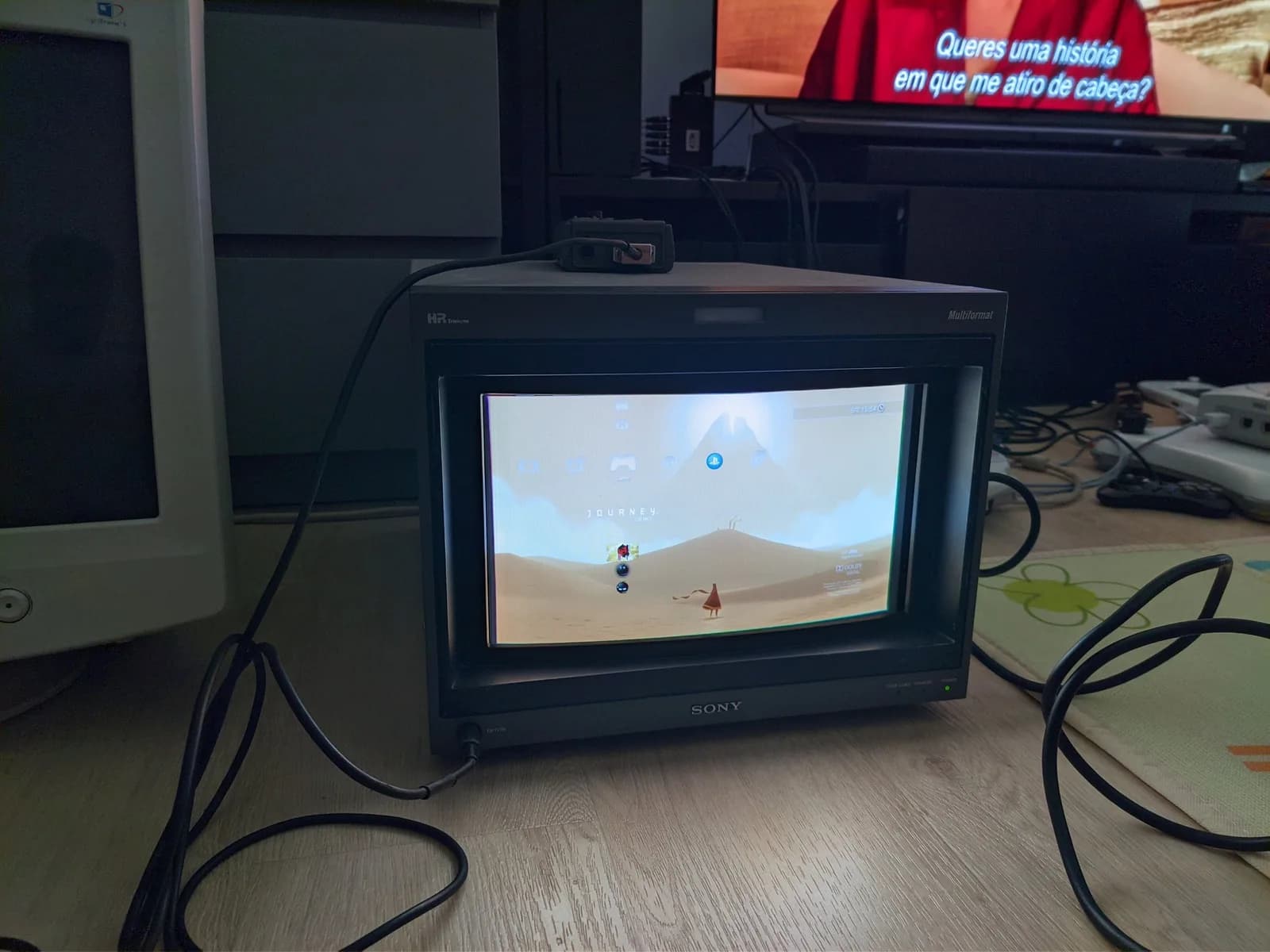 Sony BVM-D14H1E on a cluttered floor showing the PlayStation 3 XMB menu with the Journey demo highlighted, its desert artwork and robed character on screen.