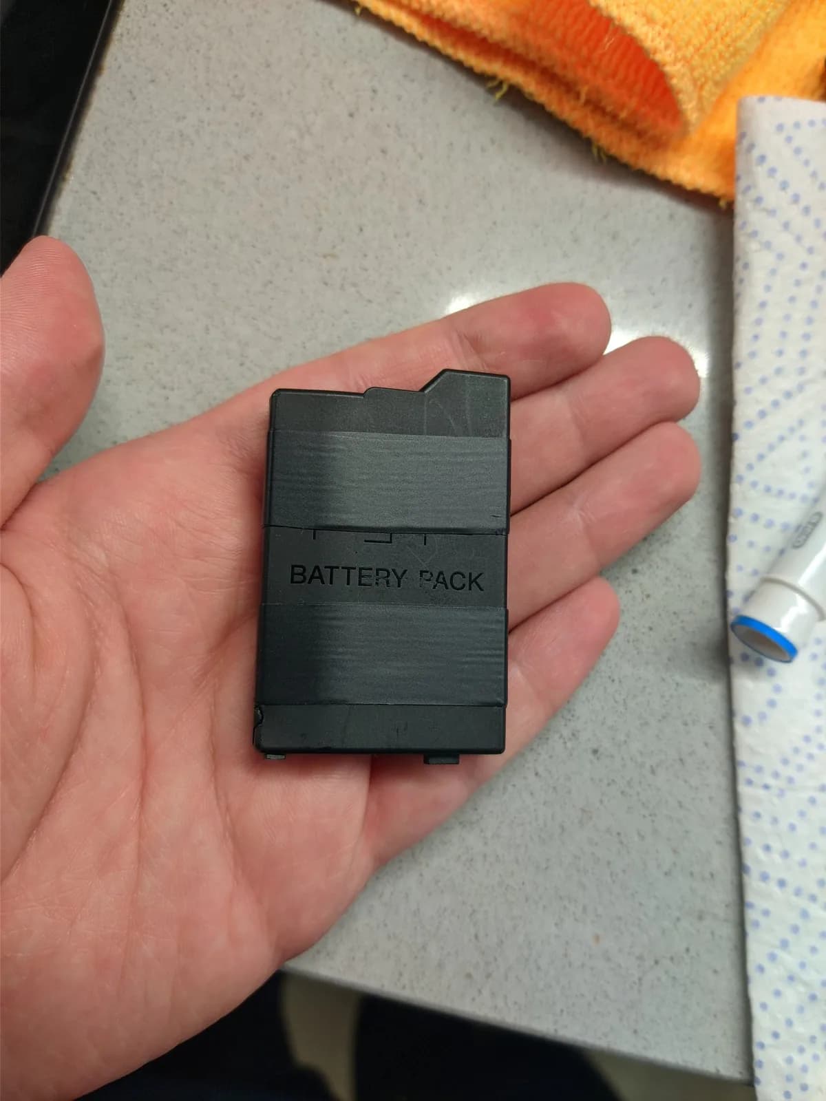 Black Sony PSP-3000 battery pack labeled "BATTERY PACK" held in hand over work surface with tools nearby.