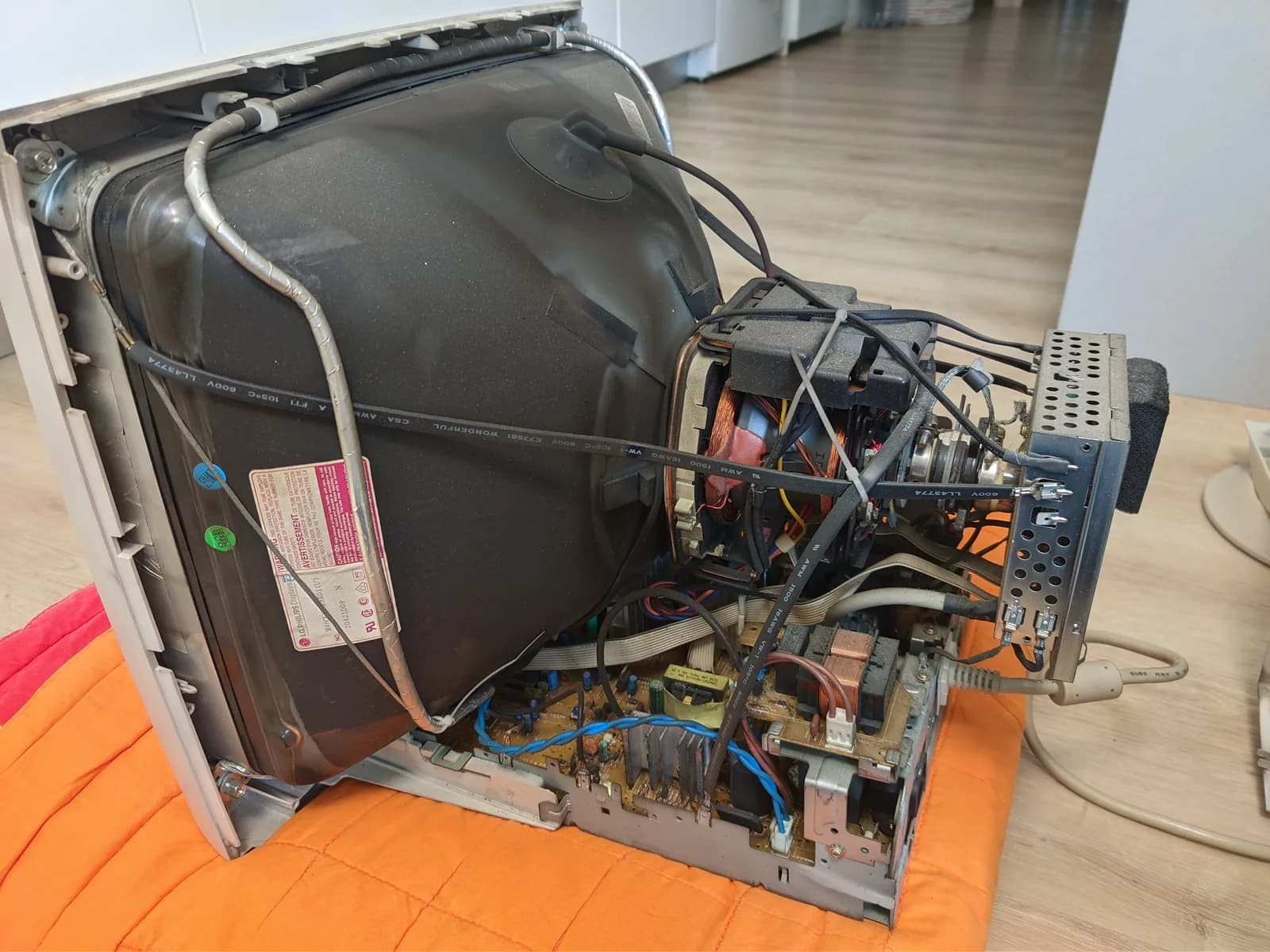 The deshelled Philips 109S4 standing in its normal upright display position on an orange moving blanket, its CRT tube, copper deflection yoke and main power-supply board (with metal heat sink) exposed, grimy with dust and nicotine.