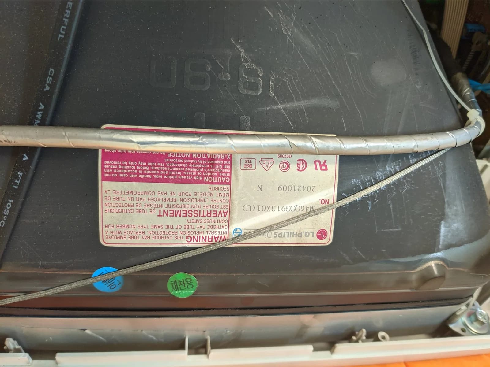 Close-up of the CRT tube's rear glass with its "LG.Philips Displays" warning / spec label (tube no. M46QCG913X01) and the spiral-wrapped degaussing cable running across it.
