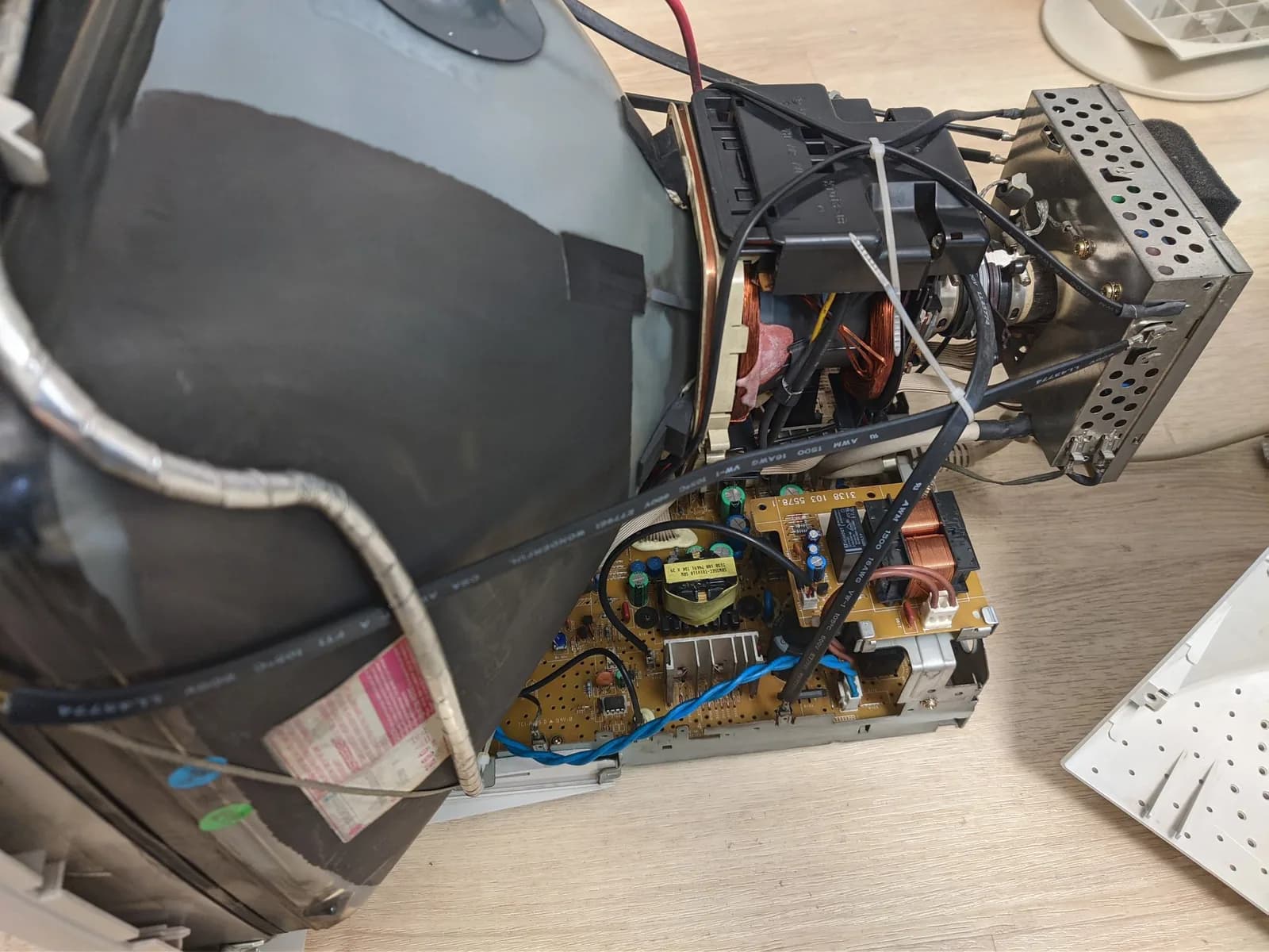 Disassembled Philips 109S4 showing the tan power-supply board (blue and green electrolytic capacitors, a yellow TDK transformer, a copper choke) alongside the deflection yoke and tube neck, whose neck board is fully encased in a metal shell.