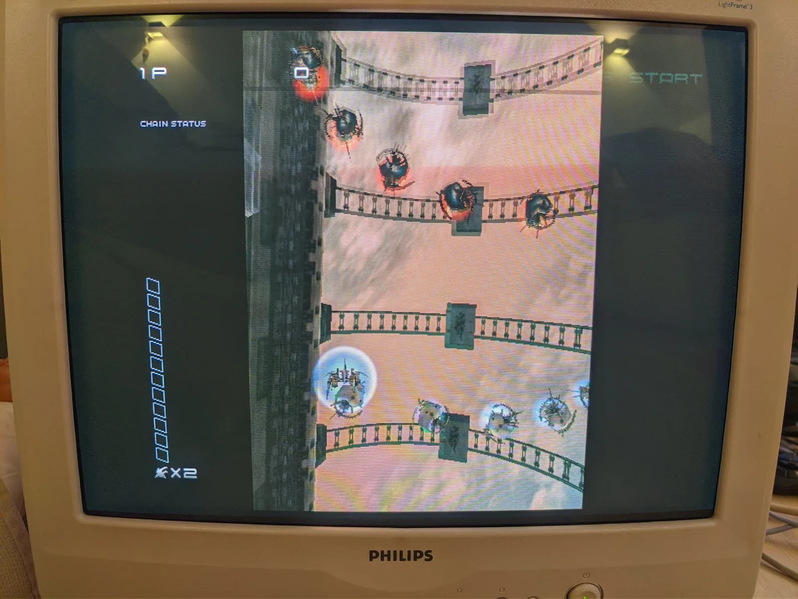 Philips 109S4 shadow-mask CRT running Ikaruga on Dreamcast, the vertical shmup playfield with enemy ships, the 1P CHAIN STATUS gauge and an x2 chain multiplier.