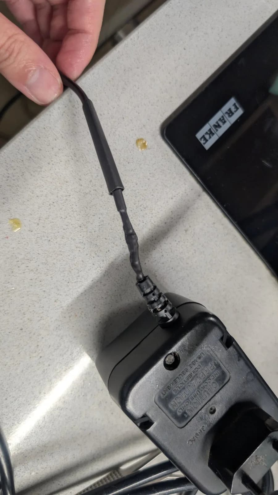 Game Gear antenna with visible solder joint repair work, held over work surface with tweezers and multimeter nearby.