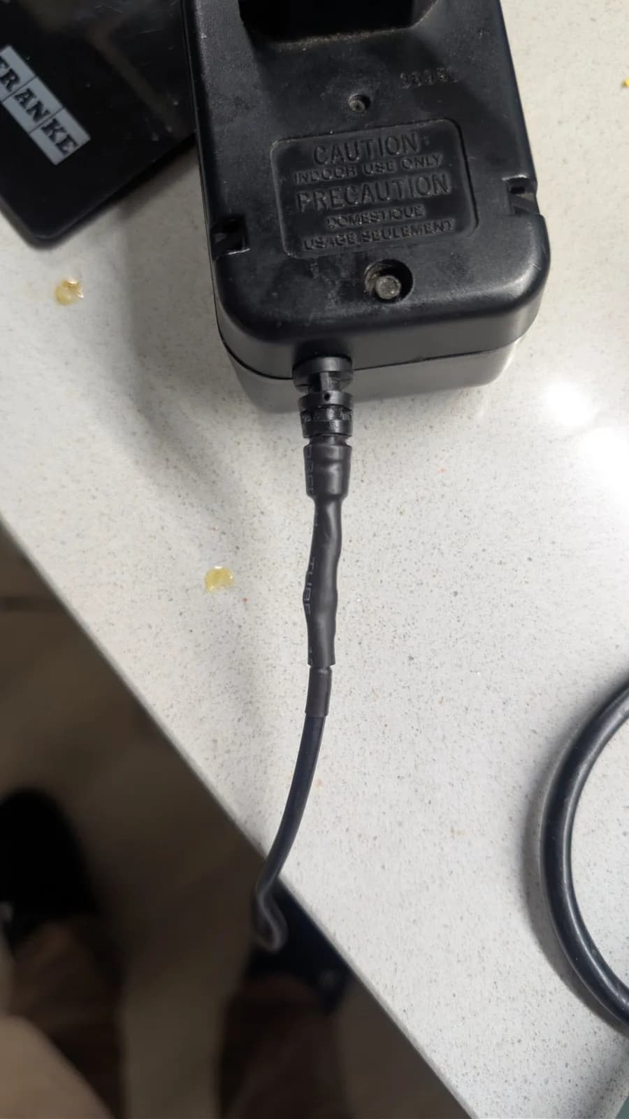 Black power adapter with "CAUTION" warning label and coiled cable on light surface during Game Gear repair.