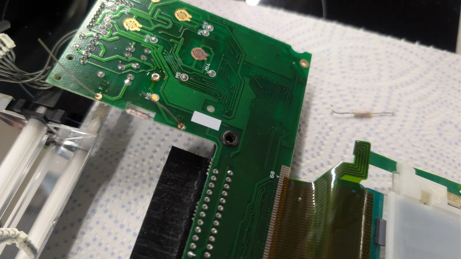 Close-up of Game Gear main board showing replaced fuse; various surface-mount components and solder joints visible on green PCB.