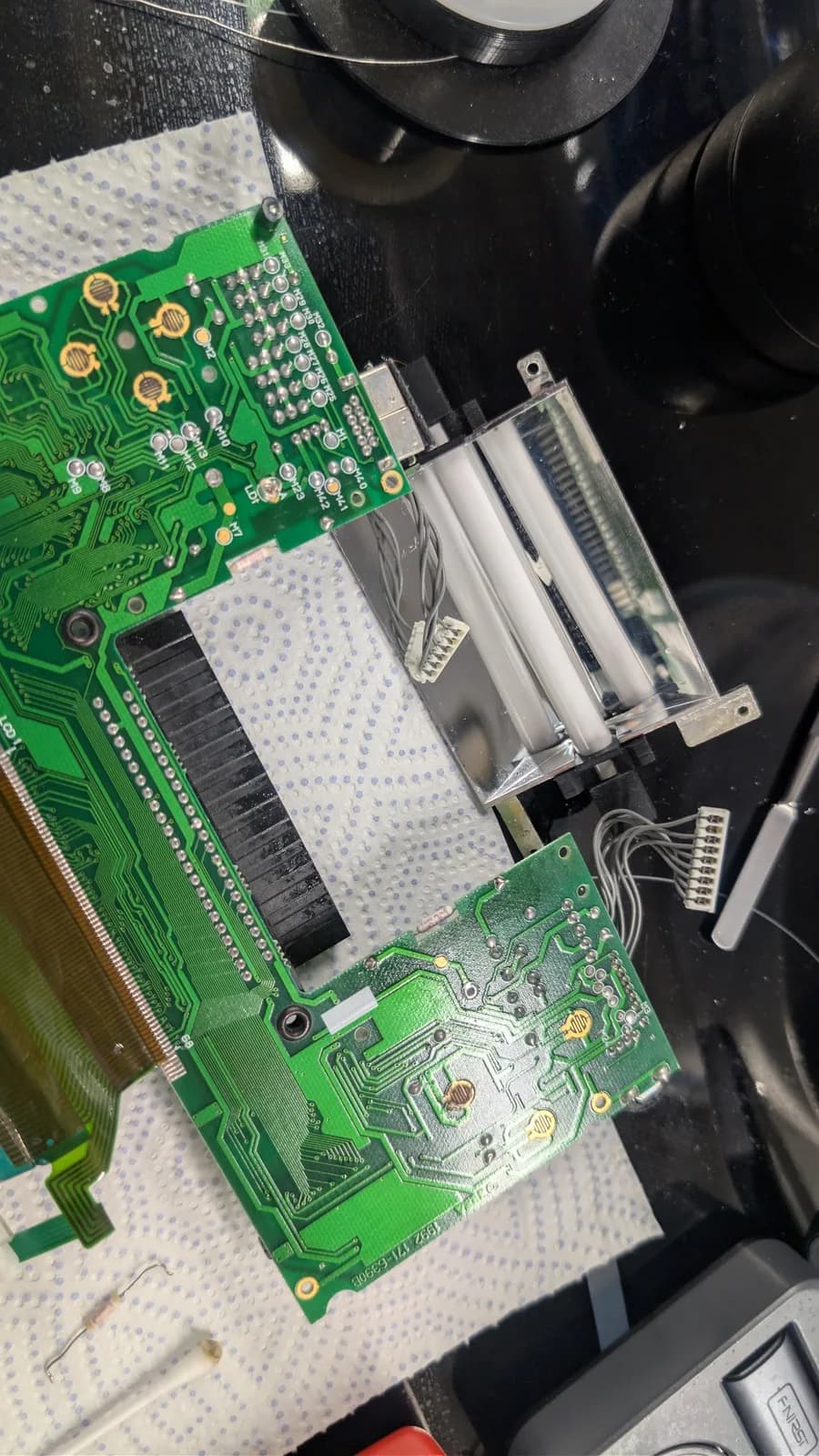 Game Gear PCB with replaced fuse; green circuit boards on white work mat with tweezers and black device above.