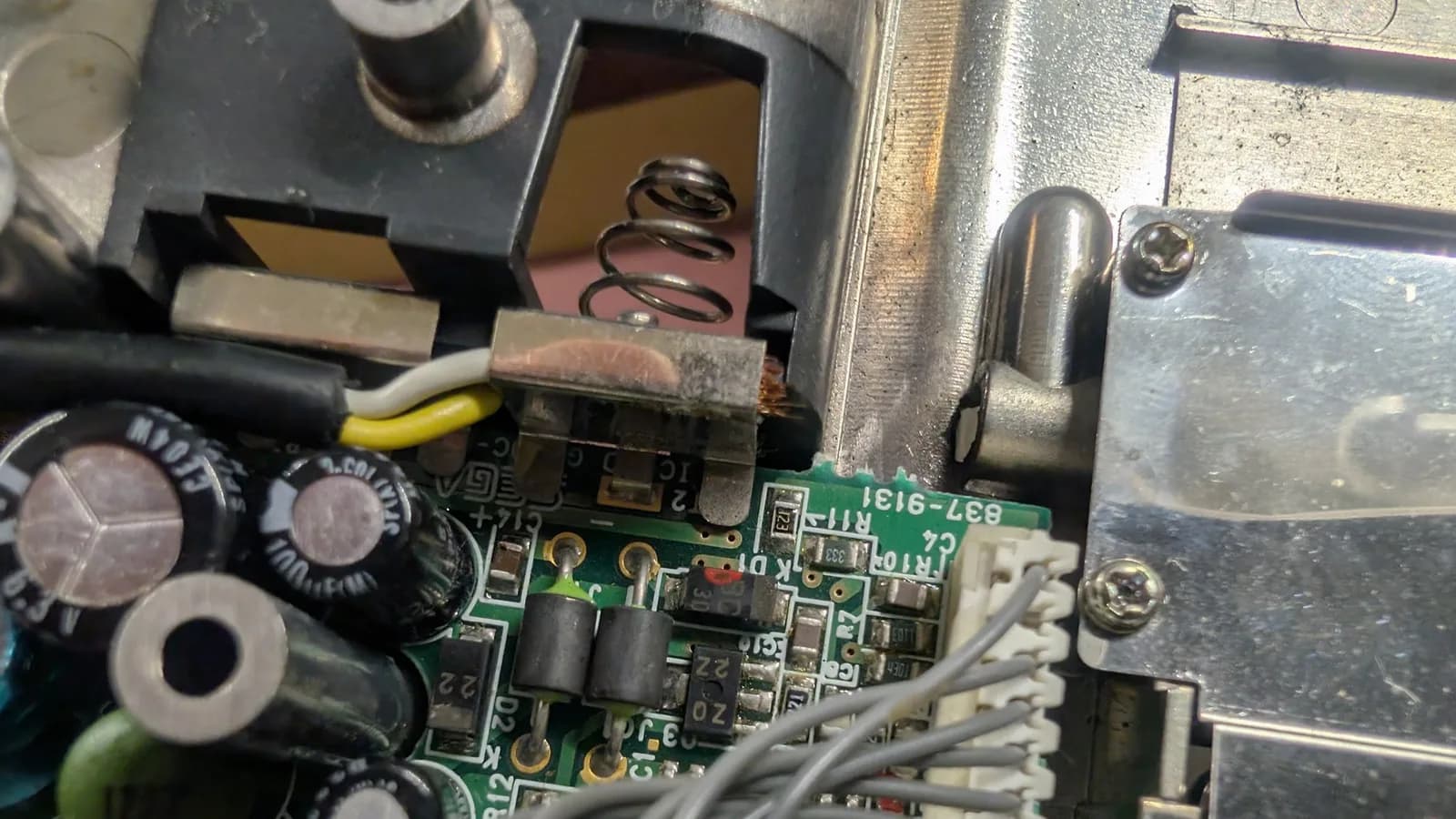 Close-up of Game Gear power supply board showing corroded metal contacts, leaking capacitors, and dangerous bodge wiring creating fire hazard.