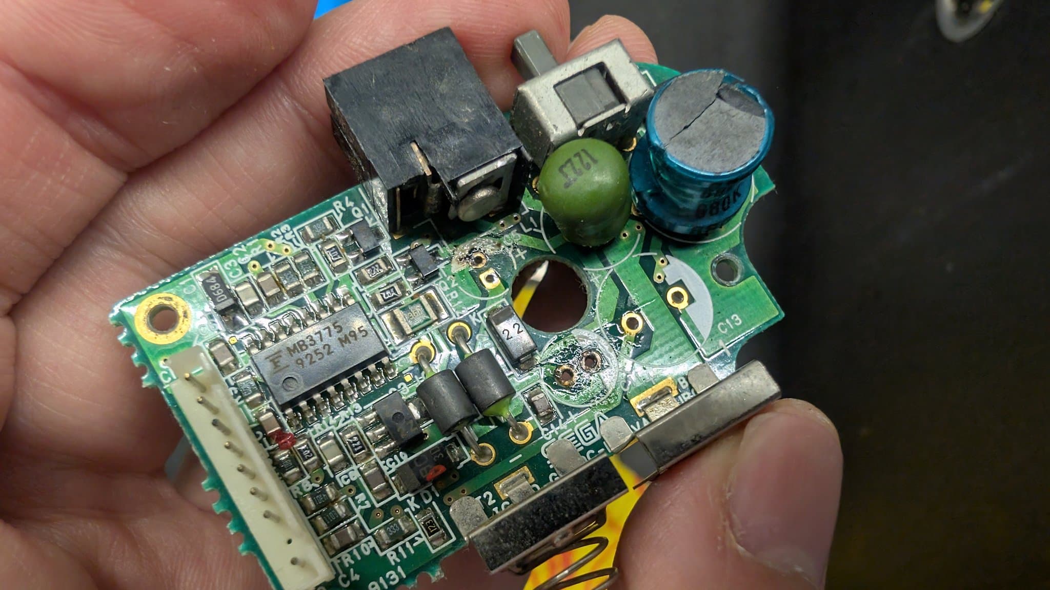 Game Gear power board held in hand showing broken solder joints at power jack after vinegar dip cleaning process.