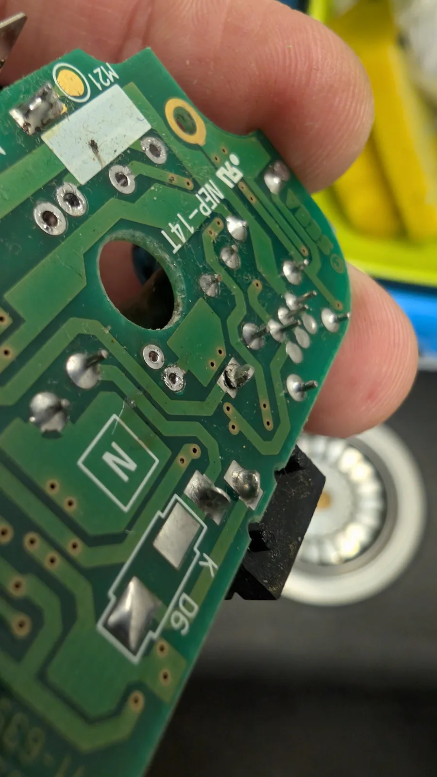 Sega Game Gear PCB held in hand showing broken solder joints at power jack, vinegar-cleaned board with visible corrosion damage.