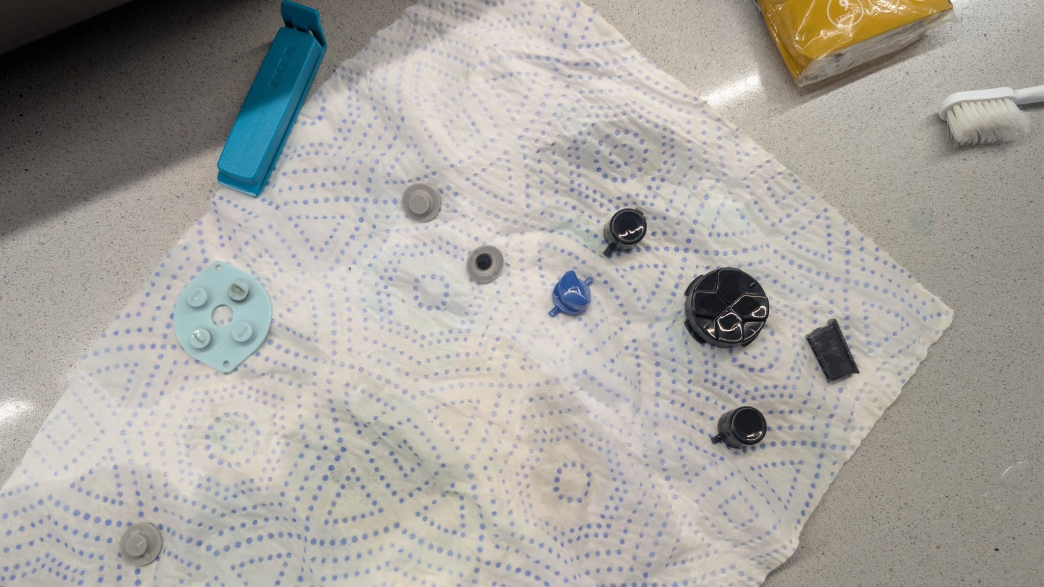 Disassembled Game Gear buttons and components laid out on dotted cloth for cleaning: rubber pad, silicone buttons, springs, and plastic casings.