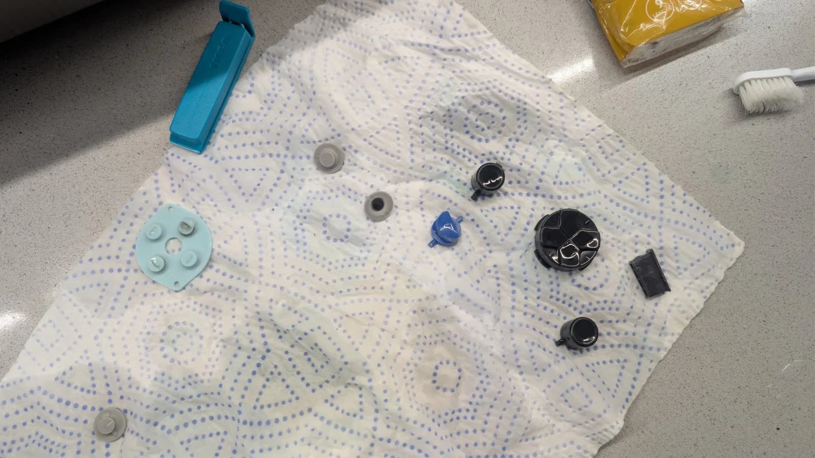 Disassembled Game Gear buttons and components laid out on dotted cloth for cleaning: rubber pad, silicone buttons, springs, and plastic casings.
