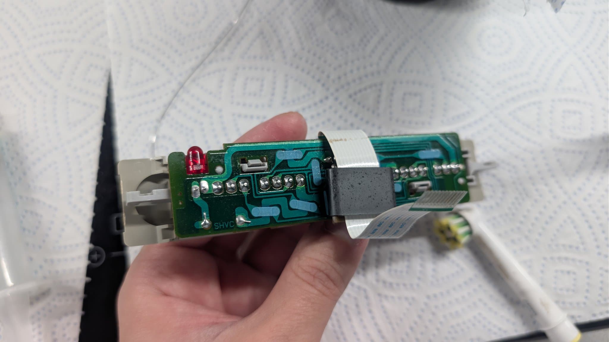 Hands holding open Super Famicom circuit board showing replaced voltage regulator, new capacitors, and touched-up solder joints on power connector area.
