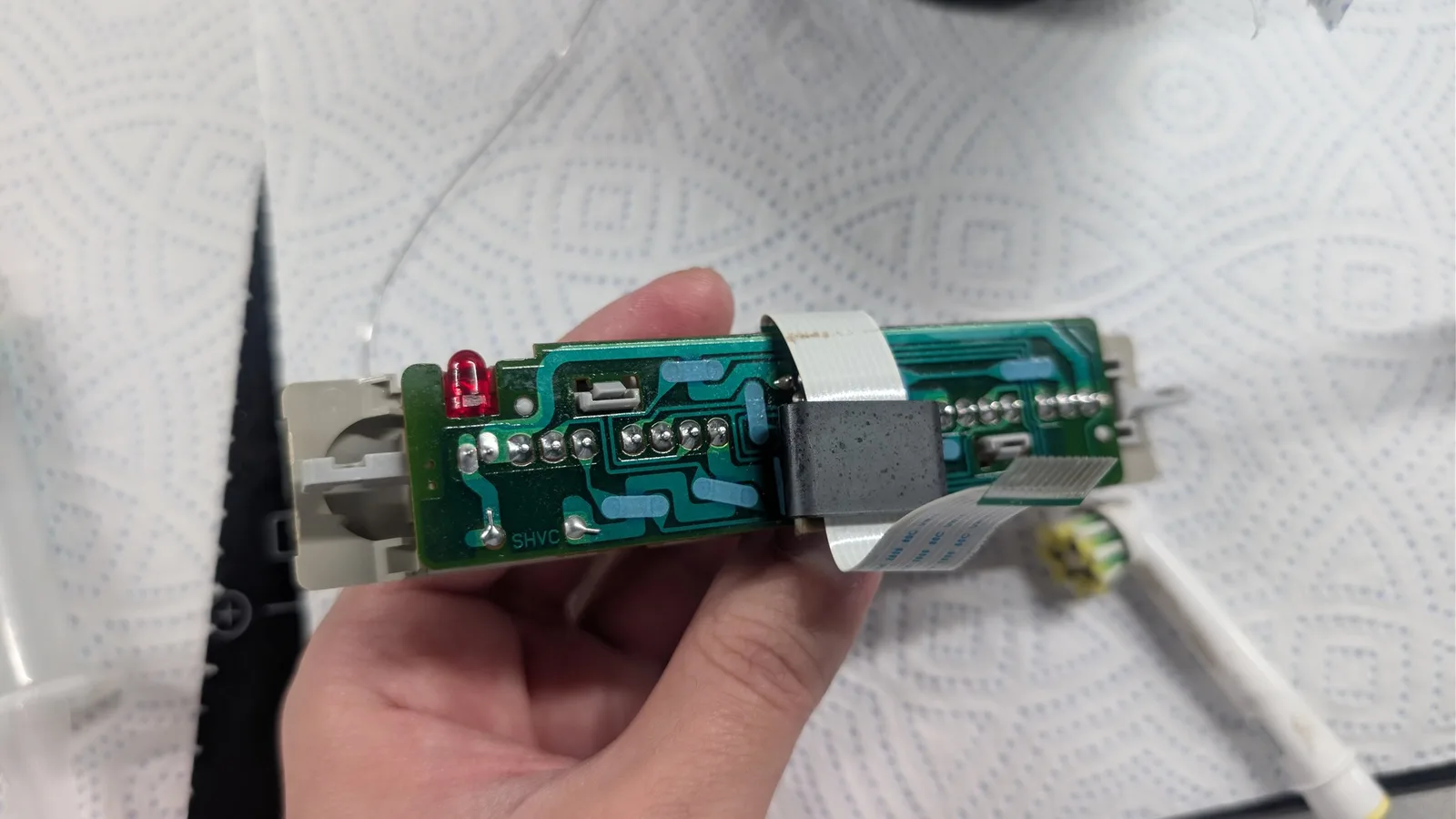 Hands holding open Super Famicom circuit board showing replaced voltage regulator, new capacitors, and touched-up solder joints on power connector area.