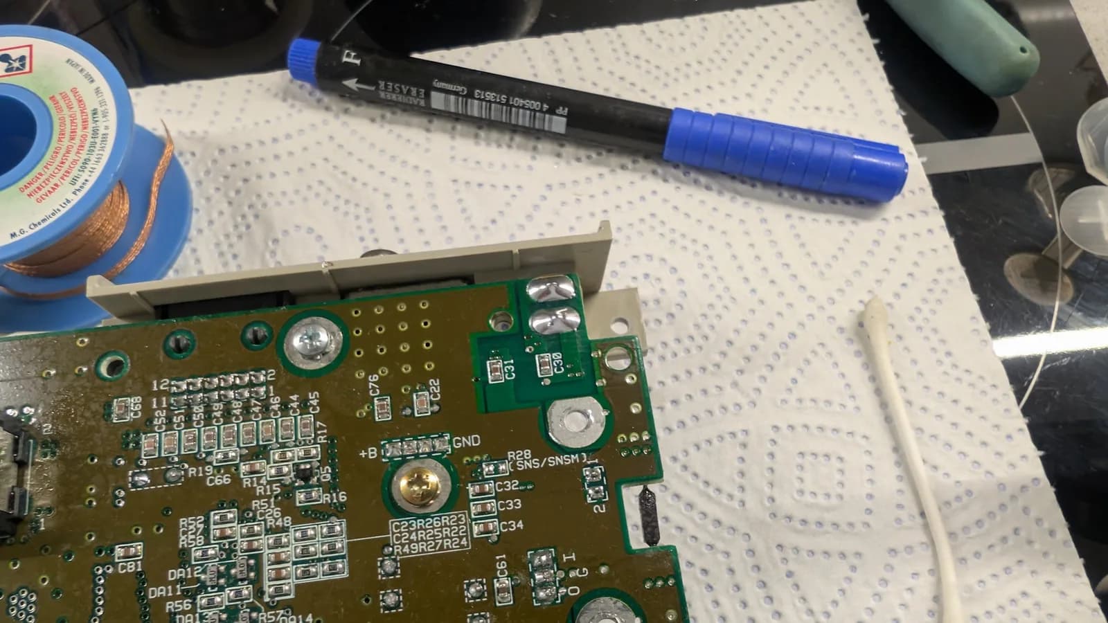 Close-up of Super Famicom PCB with replaced voltage regulator and capacitors. Blue marker pen and solder work visible on board during recapping repair.