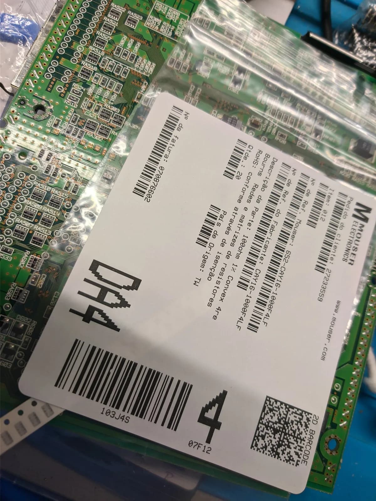 Close-up of the Sega Dreamcast VA0 motherboard's resistor-array area resting on a Mouser bag of Bourns resistor arrays (label CAY16-1000F4LF, 100 ohm), the parts for the VA0 mod that drops the GD-ROM connector voltage from 5V to the 3.3V the GDEMU needs.