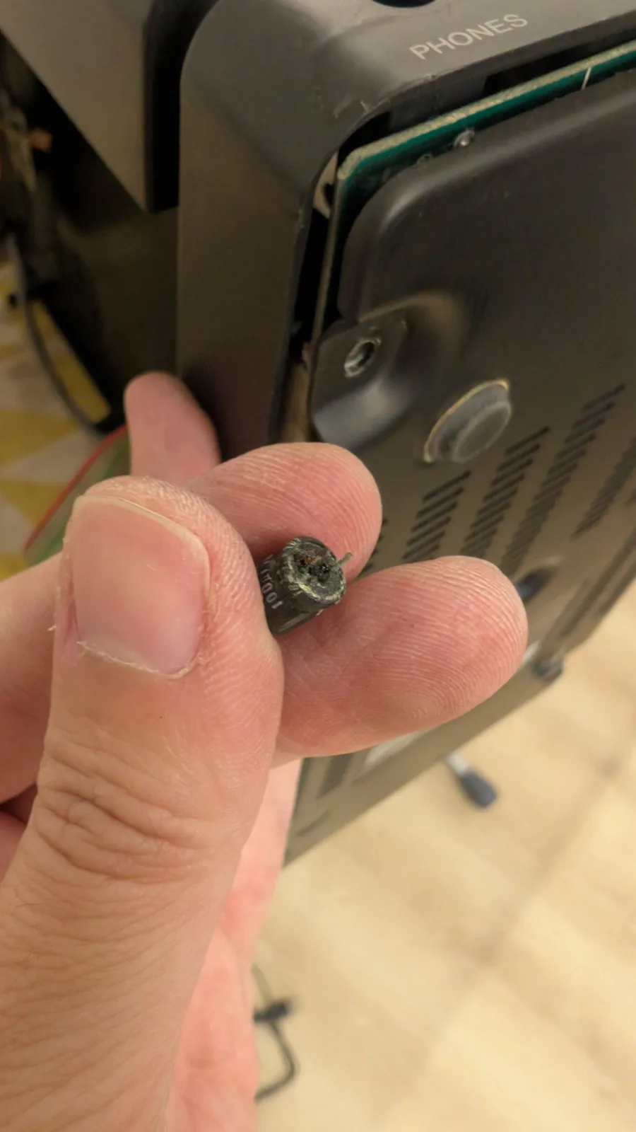 A hand holding the loose dark cylindrical capacitor found rolling around inside the Sharp X68000 case; it later turned out to have exploded off the FDD controller board, leaving black soot there.
