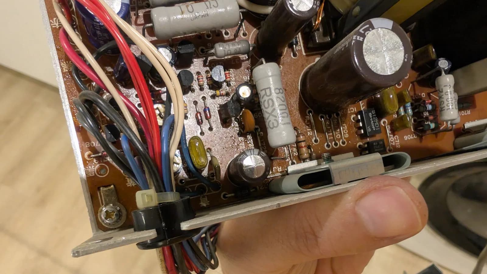 The Sharp X68000 PSU board with a bulging capacitor and electrolyte residue before recapping, a finger holding the side of the metal case the board sits in.