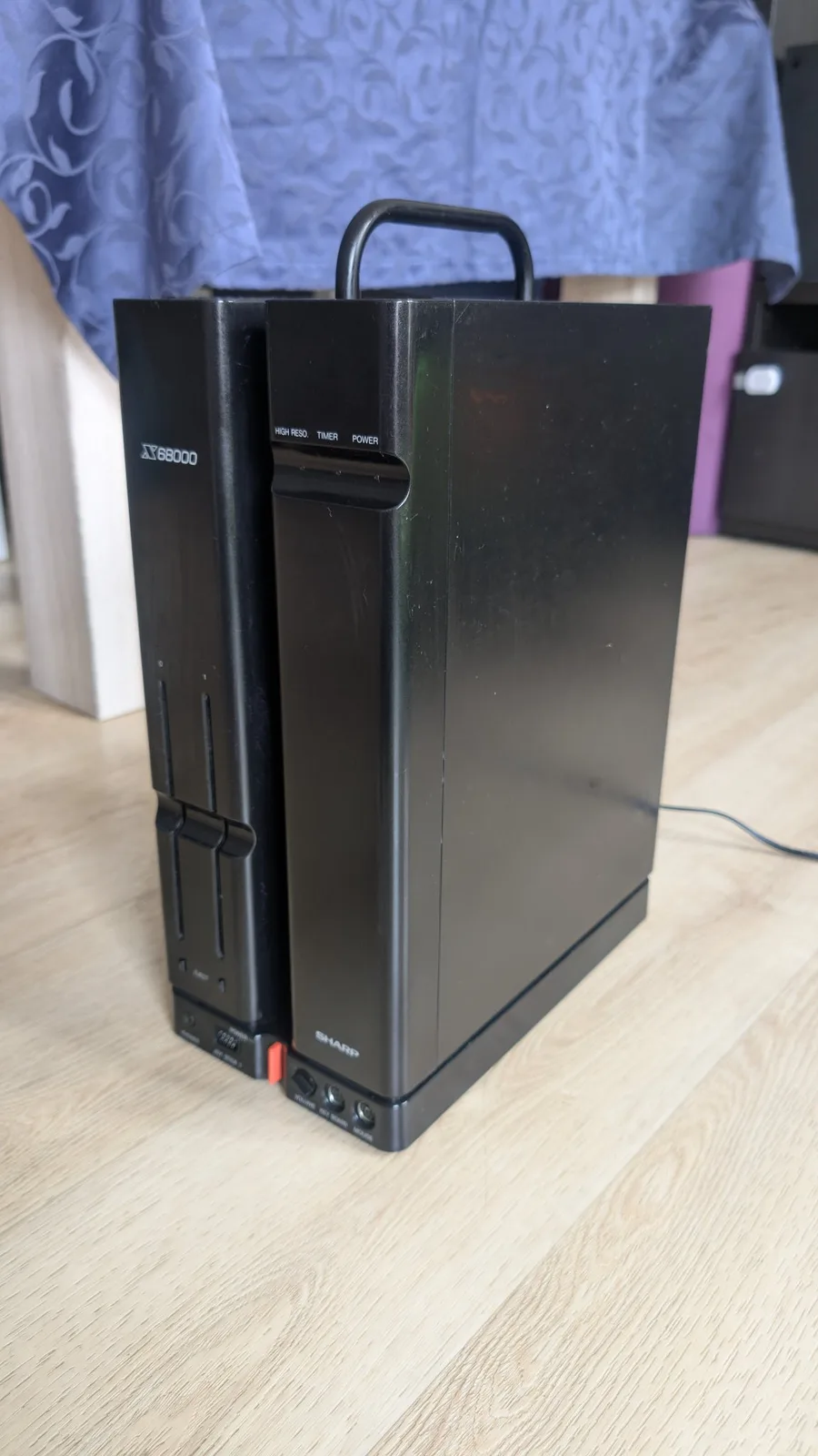The reassembled Sharp X68000 in its black vertical case with carry handle on a wooden surface, the case sheen from the Aerospace 303 protectant applied during the refurb.