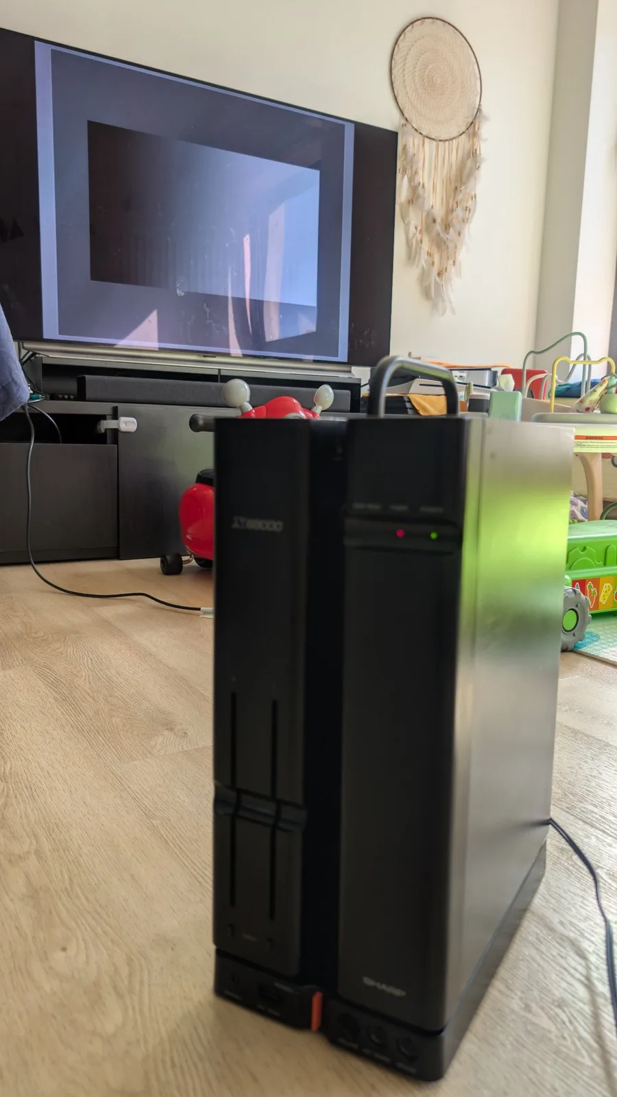 The black Sharp X68000 tower on the wooden floor, the connected monitor still showing no picture despite the machine being powered on.