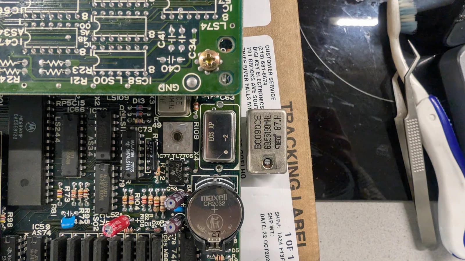 Close-up of the Sharp X68000 main board after the oscillator replacement, the old oscillator beside the new one now installed in its footprint, with the new Maxell CR2032 battery and cleaned solder joints near the battery-leak area.