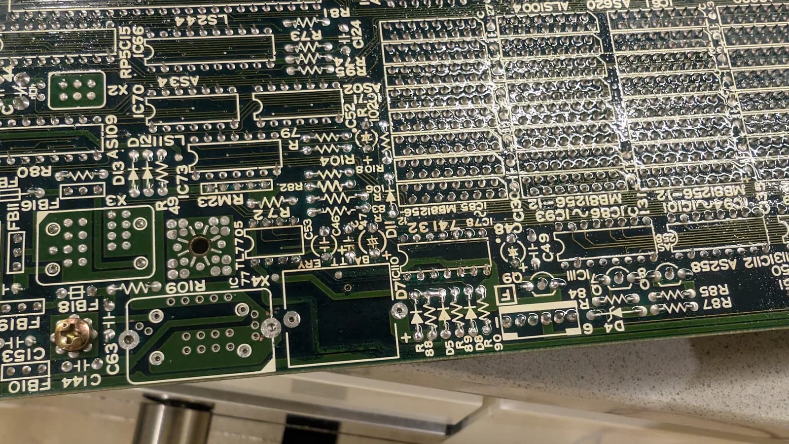 Close-up of the underside of the Sharp X68000 main board before the new battery and oscillator went in, the surrounding solder joints shiny and fluxed after being reflowed to remove the battery-leakage contamination.