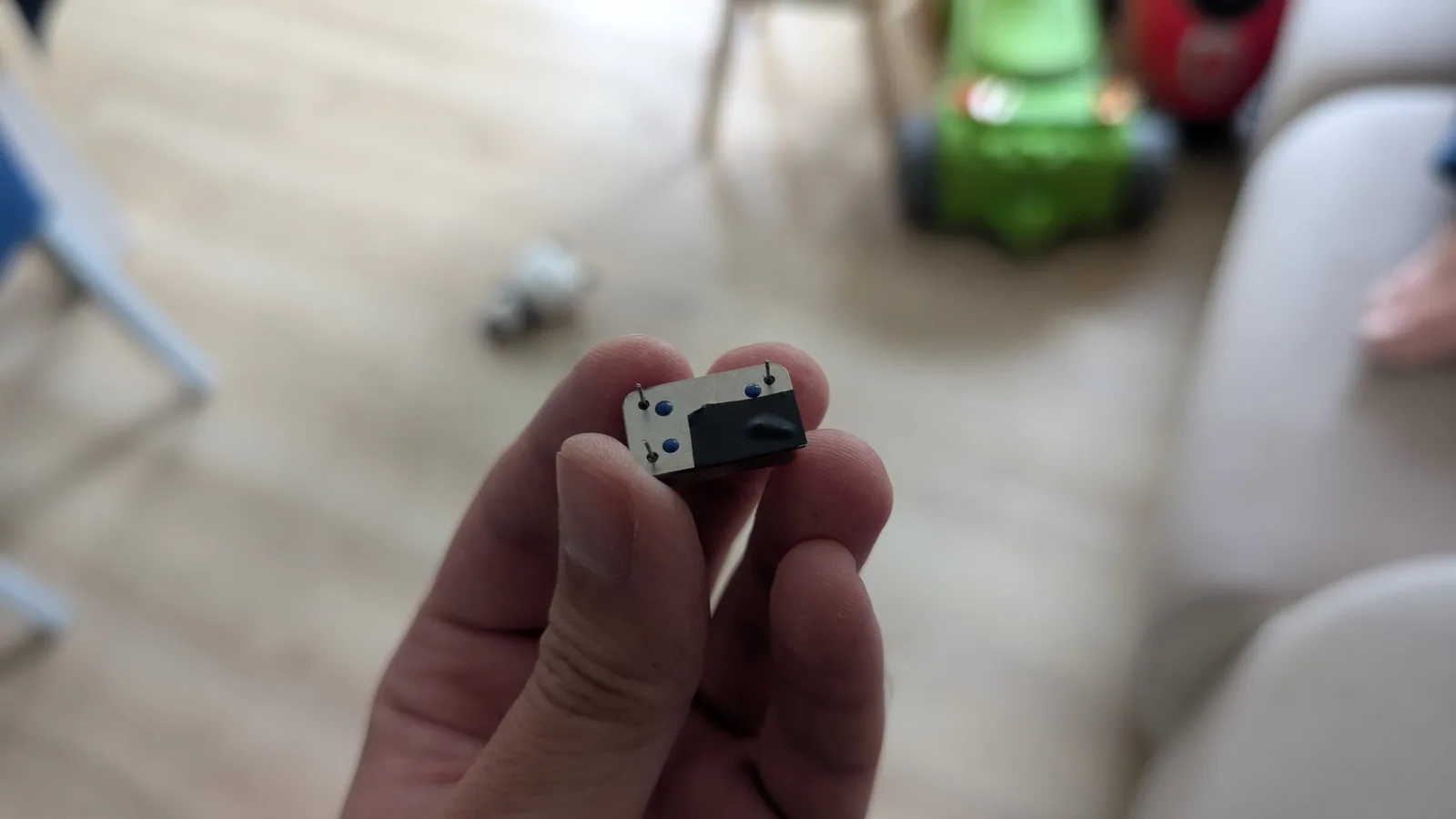 A hand holding the new oscillator with one pin snipped off, needed because that hole is tied to ground and would otherwise disable the oscillator.