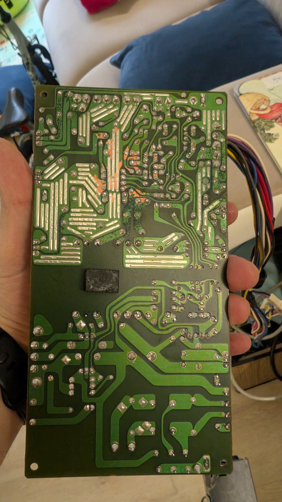 PSU PCB held in hand showing failed capacitors with oxidized solder joints and corroded component leads after ultrasonic cleaning.