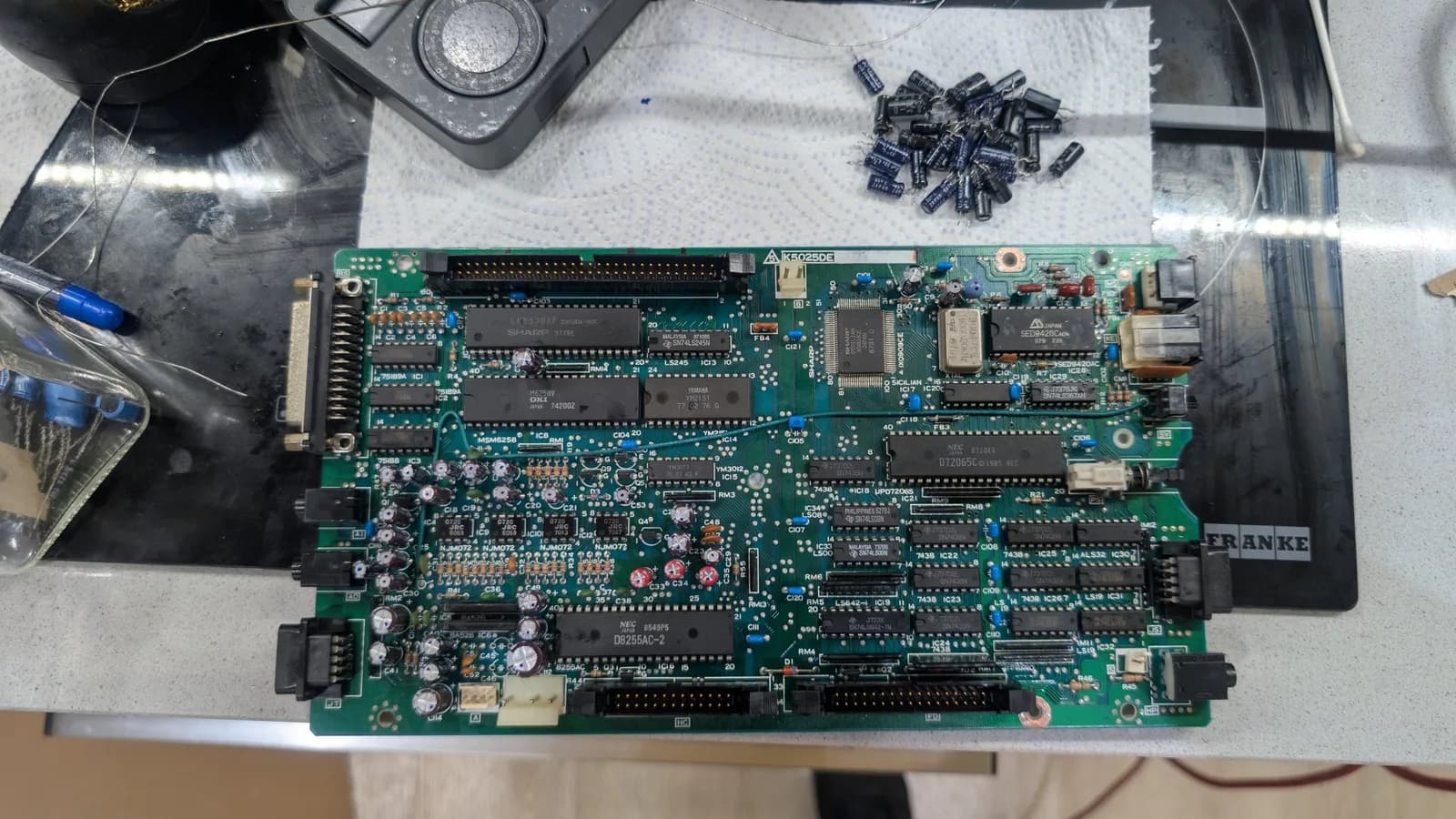 The Sharp X68000 lower board already recapped, cleaned of the white vinegar and rinsed with isopropyl, the old removed capacitors set up top.