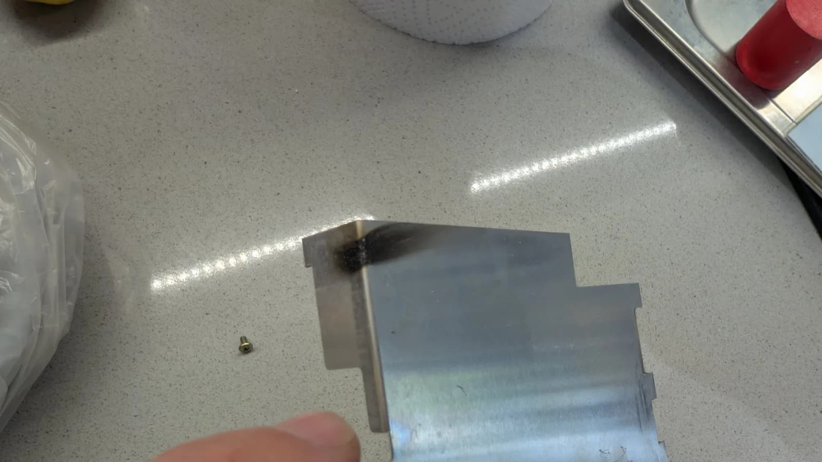 A burnt, charred metal shield on the workbench, the first sign of where something had exploded; the small item beside it is a screw, not the capacitor that caused the charring.