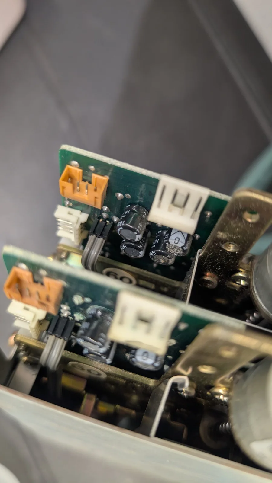 Two stacked Sharp X68000 floppy-drive controller PCBs with orange connectors, one carrying four capacitors and the other three, where the loose capacitor had blown out.