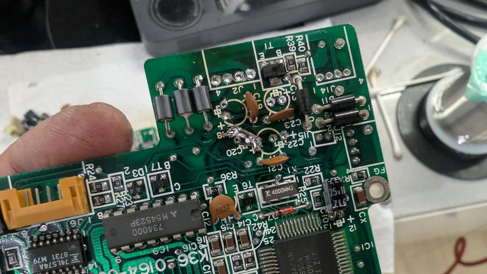 The FDD controller PCB held in a hand, showing the broken trace now patched with solder braid drenched in solder for a strong connection.