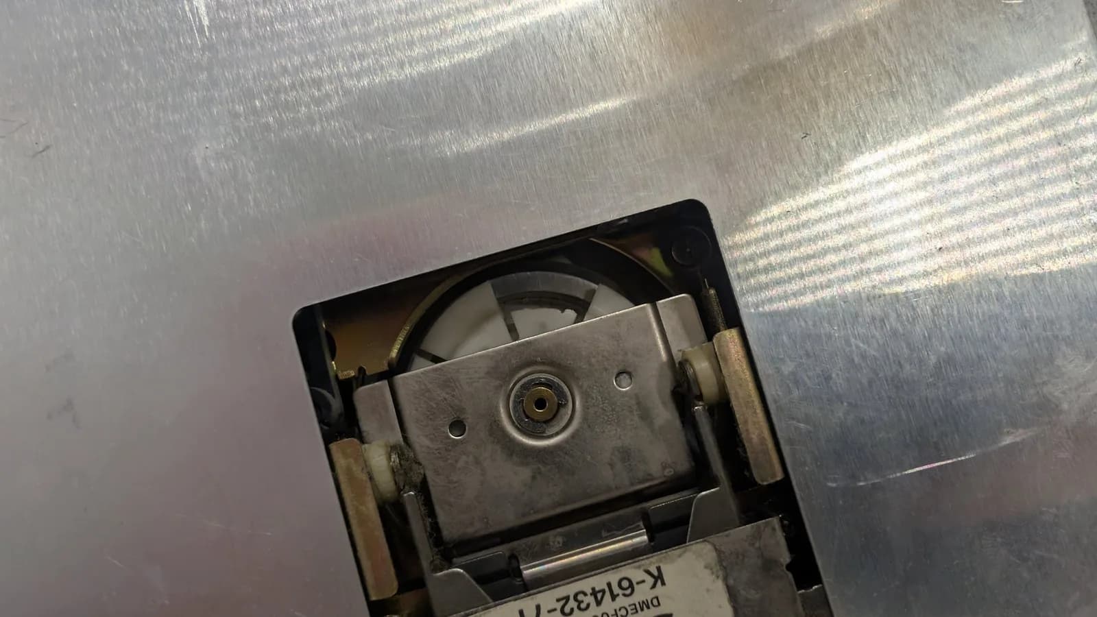 The floppy drive's metal casing around the spindle, showing the broken plastic piece of the spindle mechanism, this shot not showing where it ended up lodged.